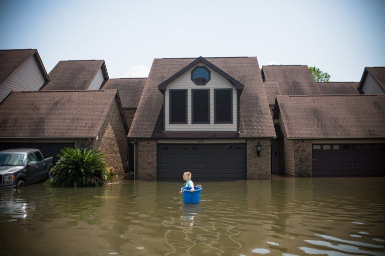 HEADING BACK HOME. Jenna Fountain carries a bucket down Regency Drive to try to recover items from their flooded home in Port Arthur, Texas, on September 1, 2017. Photo by Emily Kask/AFP   