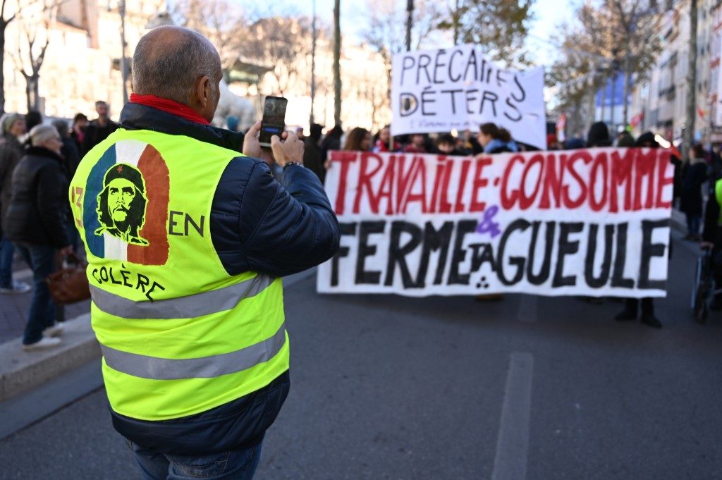 FRANCE STRIKES. A man takes a picture as demonstrators hold a banner reading 'Work, buy and shut up' as they march in Marseille, southern France, on December 10, 2019 on a sixth day of a strike of public transport operators SNCF and RATP employees over French government's plan to overhaul the country's retirement system. File photo by Christophe Simon/AFP 
