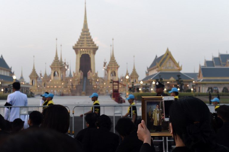 CENTER OF CEREMONIES. A mourner holds an image of the late Thai King Bhumibol Adulyadej as she takes a photo in front of the Royal Crematorium before the royal cremation ceremony in Bangkok on October 26, 2017. Lilian Suwanrumpha/AFP 