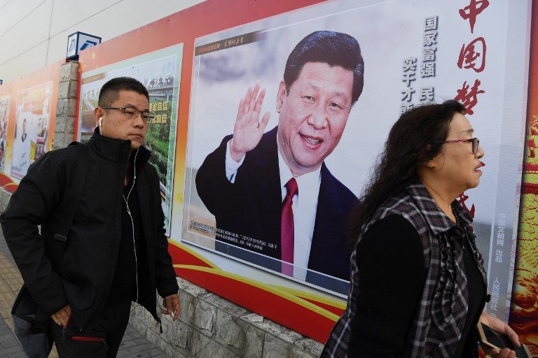 CULT OF PERSONALITY? People walk past a poster of Chinese President Xi Jinping beside a sidewalk in Beijing, during the 19th Communist Party Congress on October 23, 2017. Photo by Greg Baker/AFP  