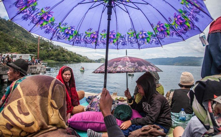 HOPING. Family members sit together as they wait for rescue teams searching for missing passengers at the Lake Toba ferry port in the province of North Sumatra on June 20, 2018, after a boat capsized on June 18. Photo by Ivan Damanik/AFP   