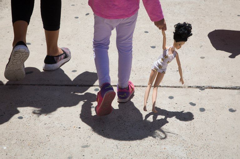 FREE FOR NOW. A 4-year-old Honduran girl carries a doll while walking with her immigrant mother, both released from detention through the 'catch and release' policy, from a Catholic Charities relief center to a nearby bus station on June 17, 2018, in McAllen, Texas. Photo by Loren Elliot/AFP   