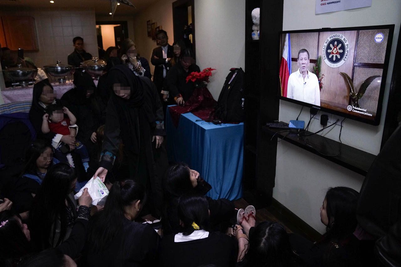 PRESIDENT'S MESSAGE. OFWs gather around to watch a video message from President Rodrigo Duterte. 