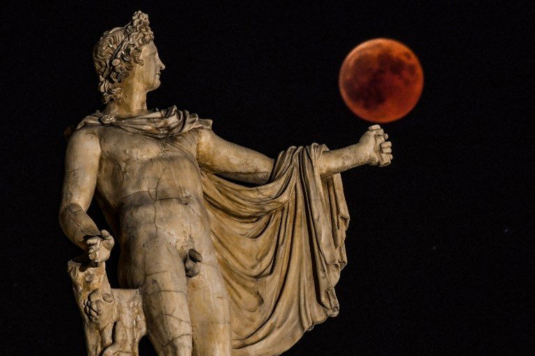 APOLLO. A picture shows the full moon during a 'blood moon' eclipse beside a statue of the ancient Greek god Apollo in central Athens on July 27, 2018. Photo by Aris Messinis/AFP 