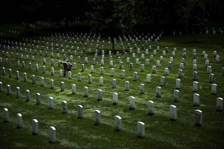 MEMORIAL DAY PREPARATIONS. A soldier in the Old Guard places flags at graves in Arlington National Cemetery during 'Flags In' in preparation for Memorial Day on May 25, 2017. Photo by Brendan Smialowski/AFP   