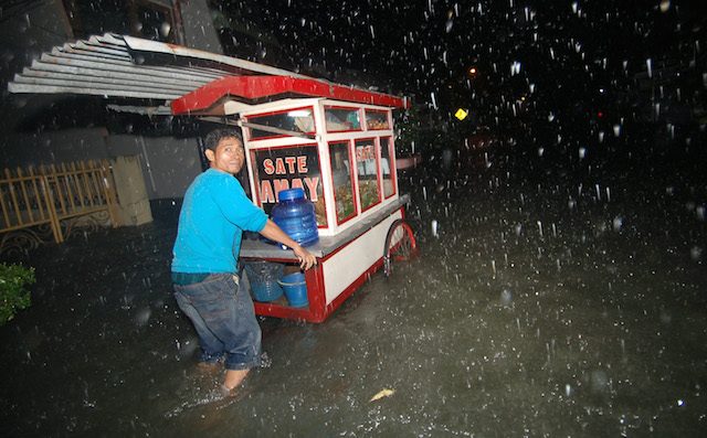 Pedagang sate melintasi banjir yang menggenangi jalan Kampung Nias, Padang, Sumatera Barat, pada 16 Juni 2016. Foto oleh Iggoy el Fitra/Antara 