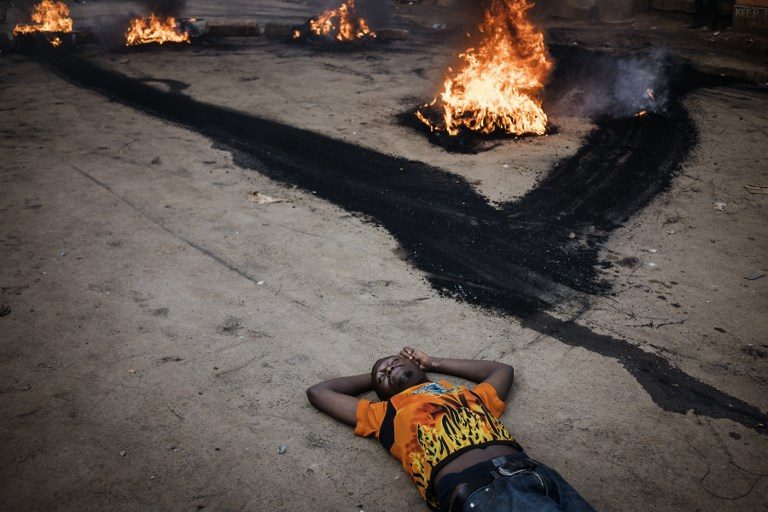 KENYA ELECTIONS. An opposition supporter lays on the street, unharmed, as he demonstrates near a burning barricade in Kibera, Nairobi, on October 25, 2017, a day before the scheduled repeat presidential poll. Photo by Marco Longari/AFP   