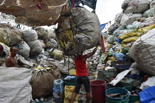 INFORMAL WORK. A worker carries a bale of collected recyclable materials at a junk shop near a former dumpsite in Manila. File photo by Ted Aljibe/AFP 