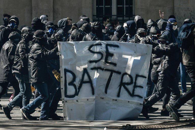 MASS DEMO. Protesters known as "black bloc" walk with a banner reading in French "to fight" during a demonstration on April 19, 2018 in Paris, as part of a multi branch day of protest called by French unions CGT and Solidaires against French President's policies amid a rail strike and spreading student sit-ins. Photo by Philippe Lopez/AFP  