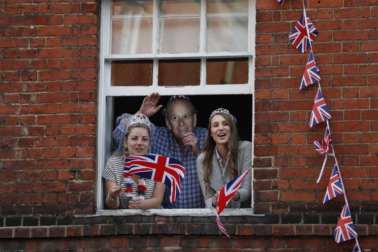 WAITING FOR THE WEDDING. Royal fans lean out of windows as they watch Britain's Prince Harry and his best man Prince William, Duke of Cambridge, greet well-wishers on the street outside Windsor Castle on May 18, 2018, the eve of Prince Harry's royal wedding to US actress Meghan Markle. Photo by Adrian Dennis/AFP  