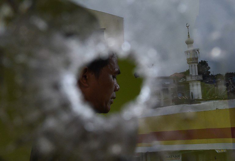PEACE TIME. A policeman prays inside a building riddled with bullet holes as a mosque is reflected on a glass window during a lull in fighting in Marawi on May 29, 2017. Photo by Ted Aljibe/AFP   