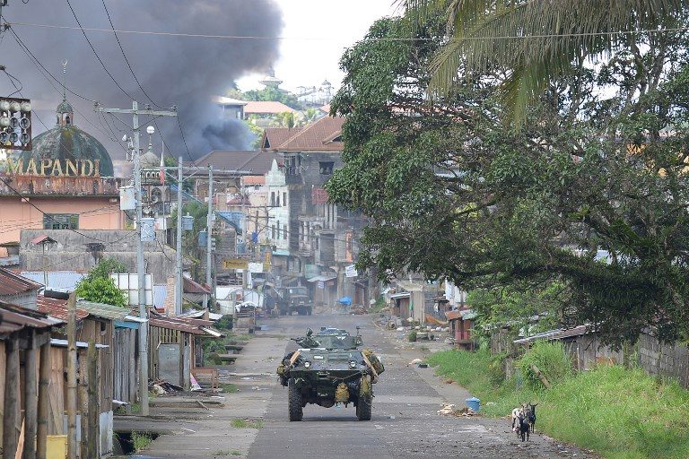 In this file photo, a Philippine Marines armored personnel carrier speeds away as black smoke billows from burning houses after military helicopters fired rockets at militant positions in Marawi on the southern island of Mindanao on May 30, 2017. Ted Aljibe/AFP 