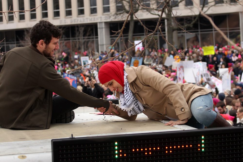 A man holds out his hand to help a Muslim woman climb up a food truck to get a better view of the rally. 