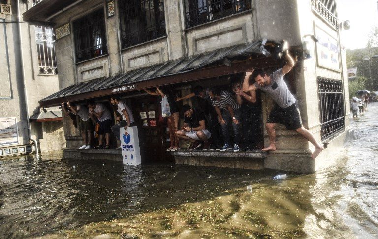 TURKEY FLOOD. Pedestrians take shelter on the window sill of a building during a heavy downpour of rain and hail in Besiktas near Istanbul on July 27, 2017. Photo by Bulent Kilic/AFP   