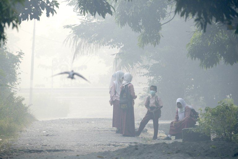 FOREST FIRE. Acehnese schoolchildren clad in masks wait for their bus to school while shrouded in thick smoke due to peat forest fires in Meulaboh, Aceh province, on July 26, 2017. Photo by Chaideer Mahyuddin/AFP   