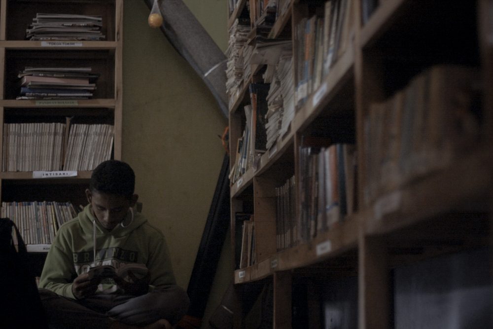 Arif nestles behind a towering bookshelf, while a book transports his mind into another world. Mick Basa / Rappler Indonesia 