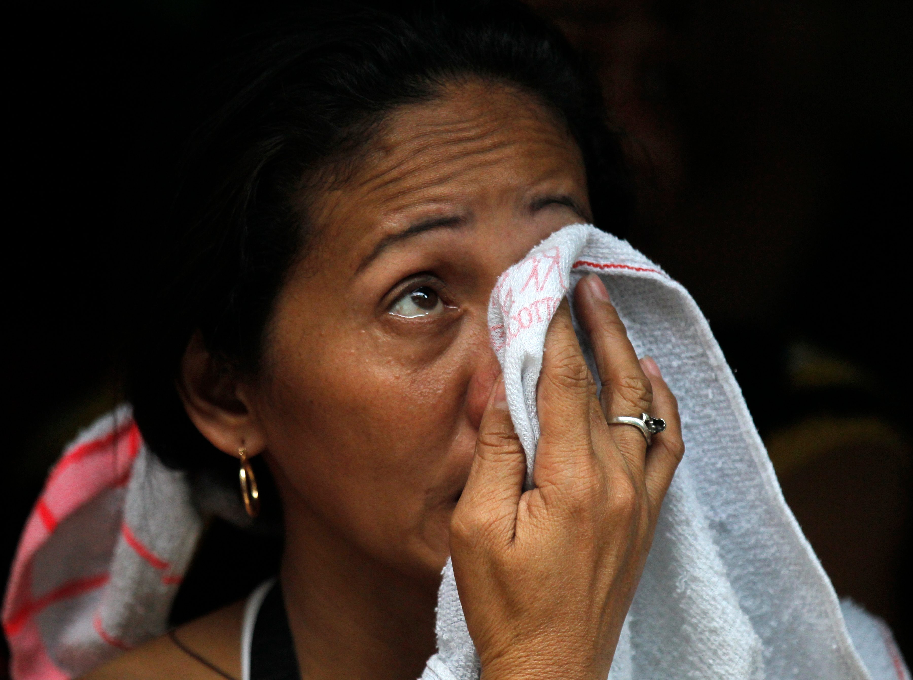 epa04745822 A Filipino relative of a missing factory worker wipes her tears following a fire at a warehouse in Valenzuela city, east of Manila, Philippines, 13 May 2015. Five persons were killed after they were trapped inside a burning rubber slipper factory in Valenzuela City, according to arson investigators from the Bureau of Fire Protection (BFP). EPA/FRANCIS R. MALASIG 