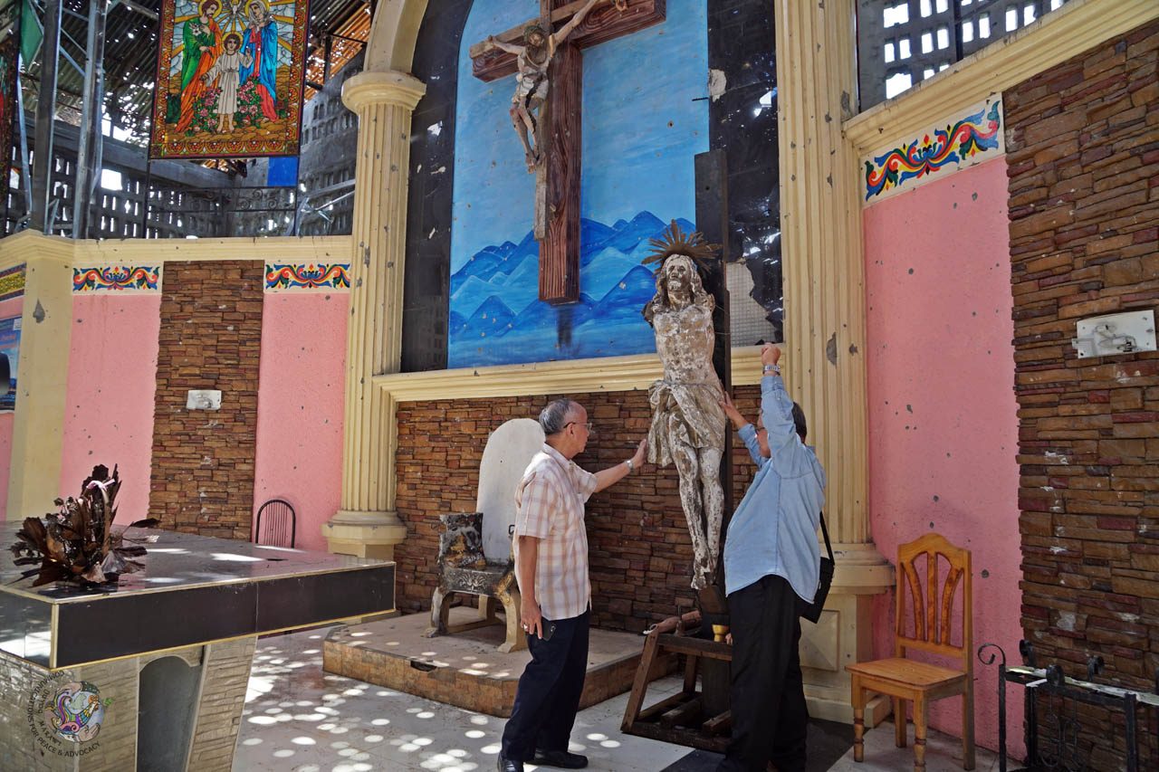 DESECRATED. Marawi Bishop Edwin De La Peña touches a broken image of Jesus Christ on the cross. Photo courtesy of DUYOG MARAWI  