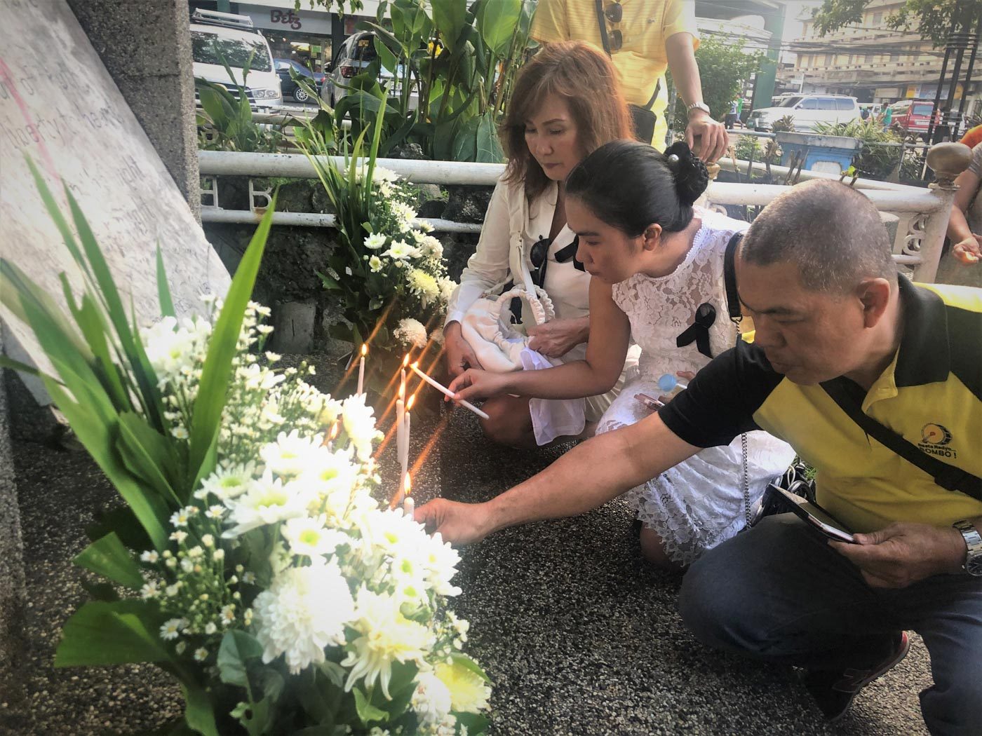 COMMEMORATION. Andrea Jayme, her daughter Hina Sofia Danielle Bianca Tugot, and Dennis Rubica of Bombo Radyo Bacolod light candles at the Marker of the Fallen Journalists at the Bacolod City public plaza on November 22, 2019. Photo courtesy of NUJP-Bacolod 