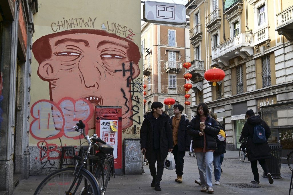 MAO. People pass by a mural depicting a Chinese face in Via Paolo Sarpi, the commercial street of the Chinese district in Milan on January 30, 2020. Photo by Miguel Medina/AFP 