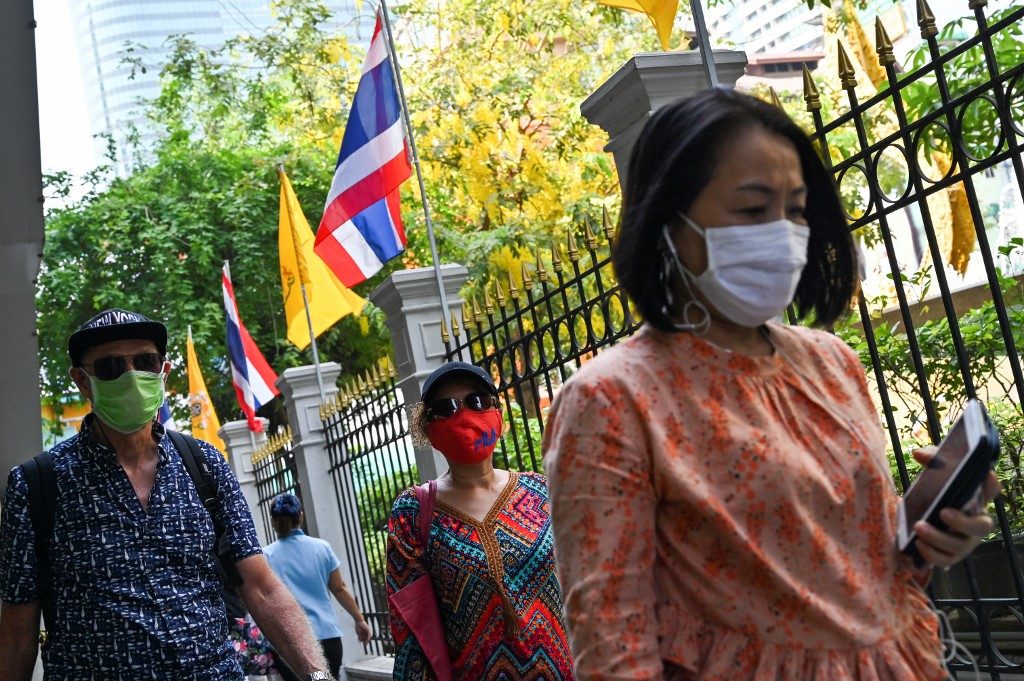 HUMAN-TO-HUMAN TRANSMISSION. People wear protective facemasks walk pass a display of Thai royal and national flags in Bangkok on January 31, 2020. Photo by Romeo Gacad/AFP 