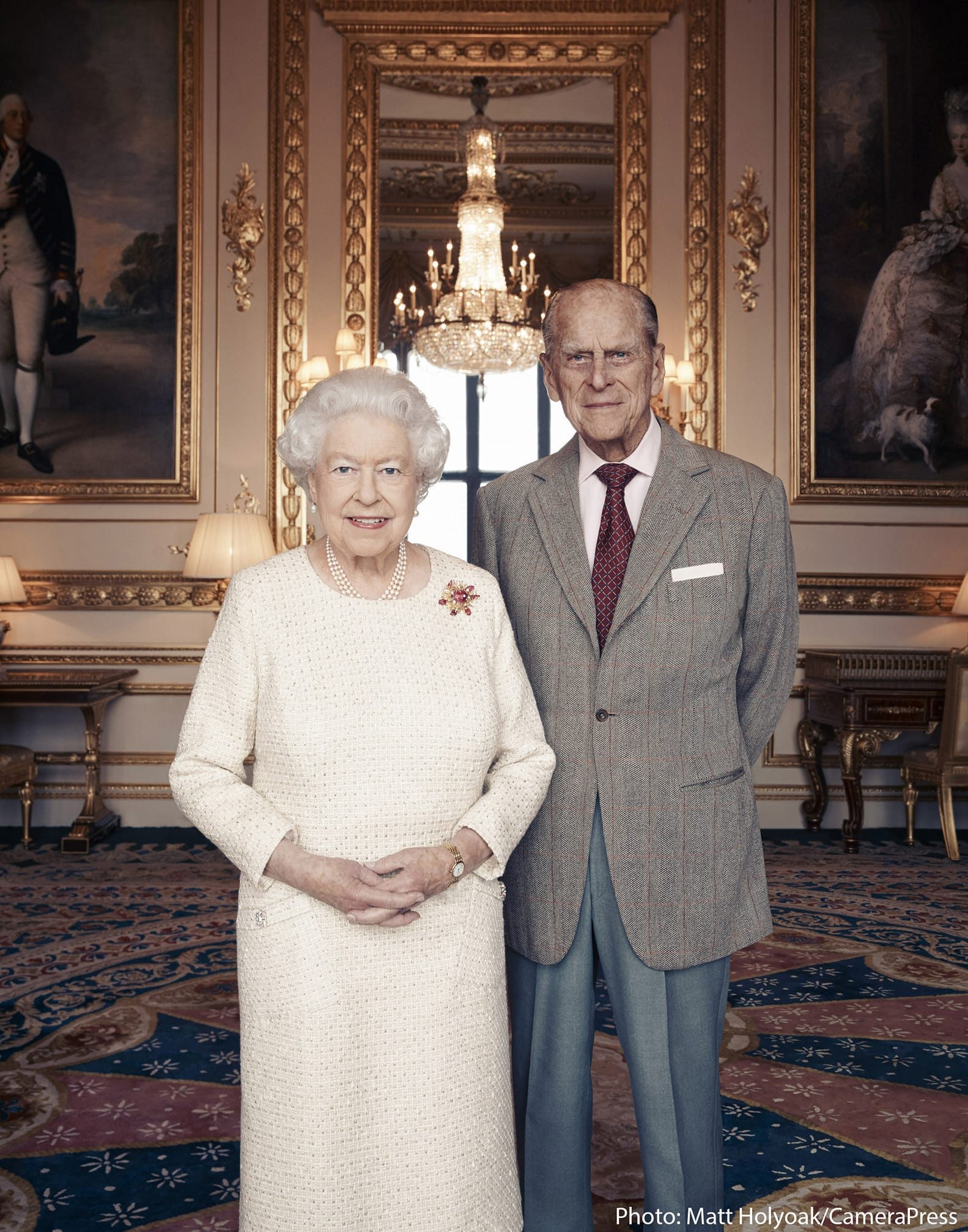 ROYAL COUPLE. In this photograph released by Buckingham Palace on November 18, 2017 and taken by Camera Press photographer Matt Holyoak in November 2017, Britain's Queen Elizabeth II and her husband, Britain's Prince Philip, Duke of Edinburgh pose between Thomas Gainsborough's 1781 portraits of George III and Queen Charlotte in the White Drawing Room at Windsor Castle, to mark their Platinum Wedding Anniversary (70 years). Matt Holyoak / CameraPress / Buckingham Palace 