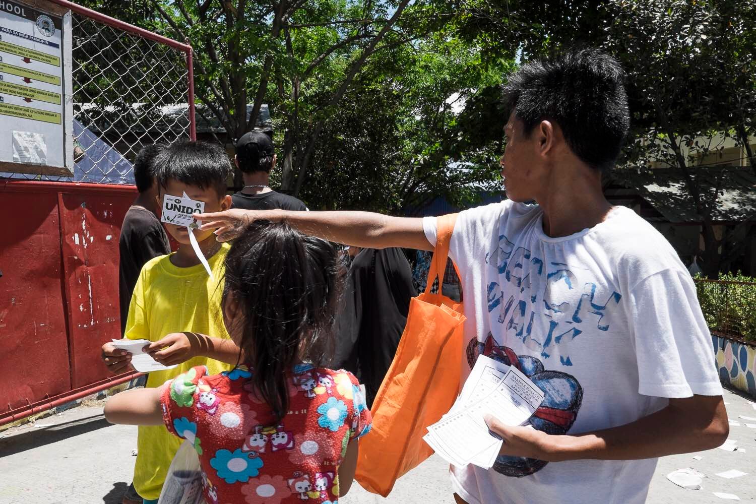 CHILDREN. Underage children are seen distributing campaign materials and sample ballots near a precinct in Taguig. Photo by Pat Nabong/Rappler  