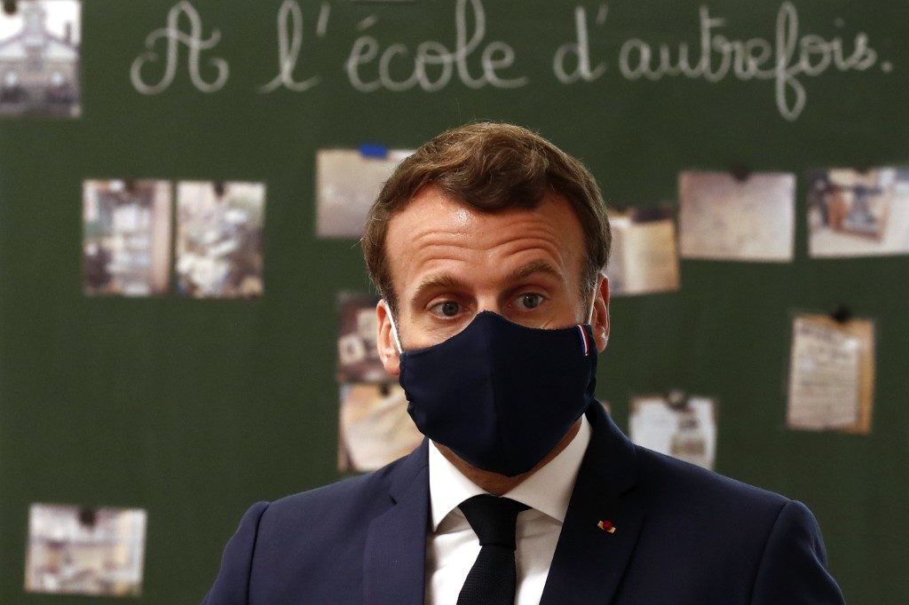FRANCE. French President Emmanuel Macron wearing a protective mask with a blue-white-red colored ribbon speaks with pupils during a visit at the Pierre Ronsard elementary school in Poissy, west of Paris, on May 5, 2020 on the 50th day of a strict lockdown in France, in place to attempt to stop the spread of the new coronavirus (COVID-19). File photo by Ian Langsdon/Pool/AFP 