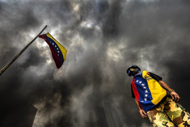 VENEZUELA CRISIS. An anti-government demonstrator stands next to a national flag during an opposition protest blocking the Francisco Fajardo highway in Caracas on May 27, 2017. Photo by Luis Robayo/AFP 