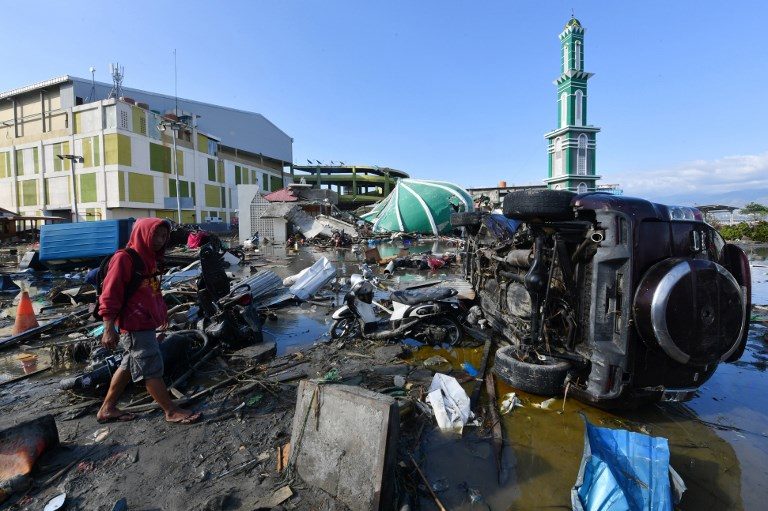 AFTERMATH. A man walks past vehicle wreckage as a collapsed mosque is seen in the background in Palu, Indonesia's Central Sulawesi on September 30, 2018, Photo by Adek Berry/AFP  
