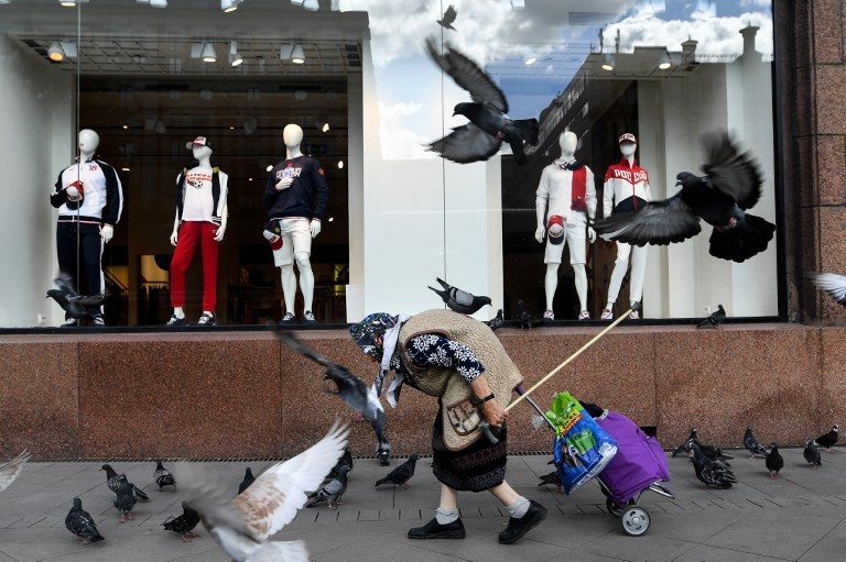 PENSION AGE. An elderly woman walks past a sports goods shop with pigeons flying around in downtown Moscow on August 8, 2018. Photo by Kirill Kudryavtsev  