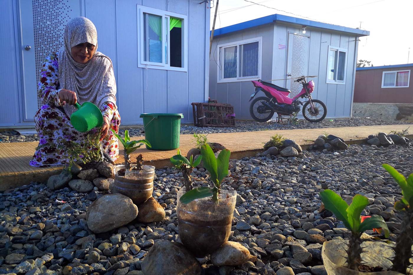 INGENUITY. A Maranao woman waters her new plants. With a little creativity, she uses larger rocks to serve as pots for her otherwise rock-covered space. She said she plans to cover her space with soil to make it more productive. Photo by Bobby Lagsa/Rappler  