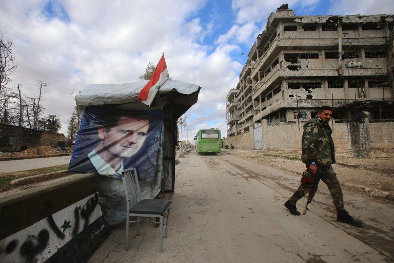A Syrian pro-government fighter patrol next to a checkpoint in the Shihan neighborhood in the government-held side of Aleppo, on December 3, 2016. A portrait of Syrian President Bashar al-Assad is seen on hanging on the booth.  Youssef Karwashan/FP 