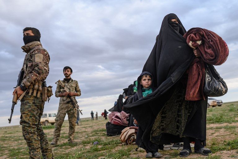 EXODUS. Member of the Kurdish-led Syrian Democratic Forces stand guard as a woman walks with a child after they left the Islamic State group's last holdout of Baghouz, in Syria's northern Deir Ezzor province on February 27, 2019. Photo by Bulent Kilic/AFP  