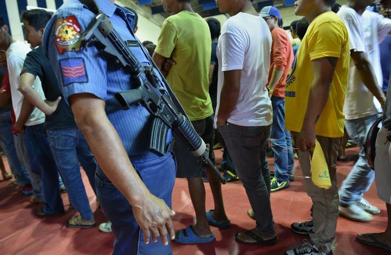 SURRENDER? A policeman stands guard as people queue to register with the police during the mass surrender of some 1,000 alleged drug users and pushers in Tanauan on July 18, 2016. Photo by Ted Aljibe/AFP   