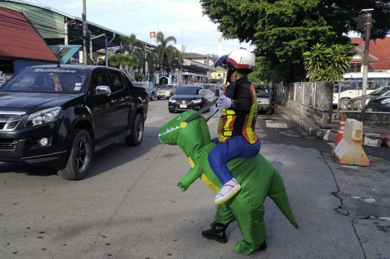 ROAD SAFETY FOR KIDS. Thai police sergeant Tanit Bussabong directs traffic wearing a costume where he appears to ride a T-rex outside a school in Nakhon Nayok on June 4, 2018. Photo by Stephen J. Boitano/AFP   