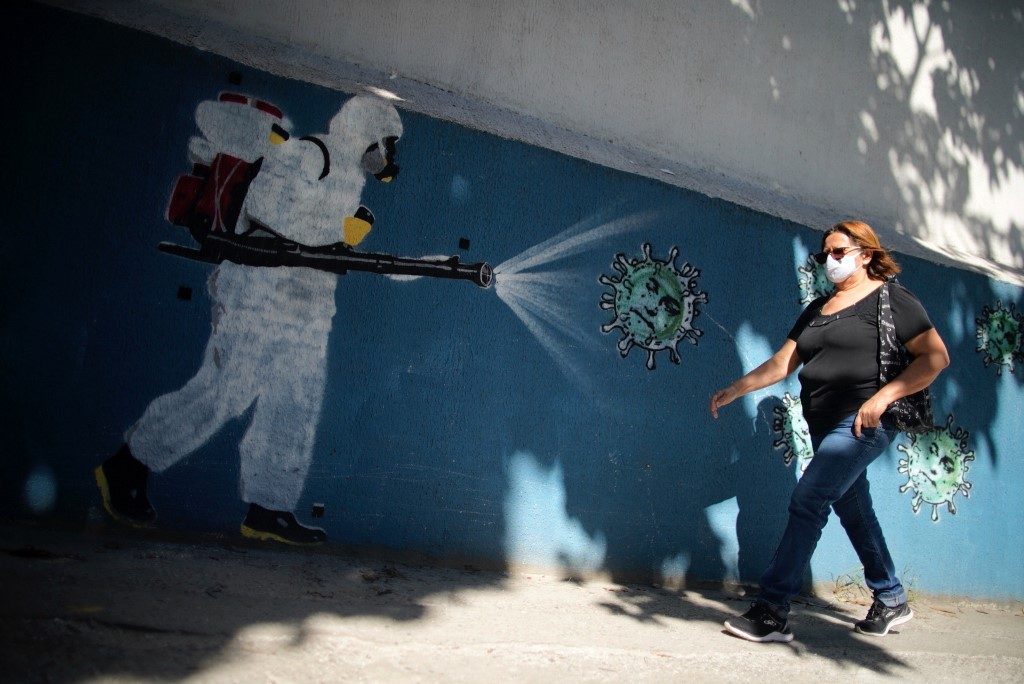 FIGHTING THE VIRUS. In this file photo taken on July 8, 2020 a woman walks in front of a mural depicting a man in protective suit spraying disinfectant on coronavirus with Brazilian President Jair Bolsonaro's face, at the Tijuca neighborhood in Rio de Janeiro, Brazil. Photo by Mauro Pimentel/AFP 